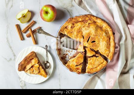 Traditional autumn apple pie cut in slices with fresh apples and demerara sugar served on a white marble background, top view, close-up Stock Photo