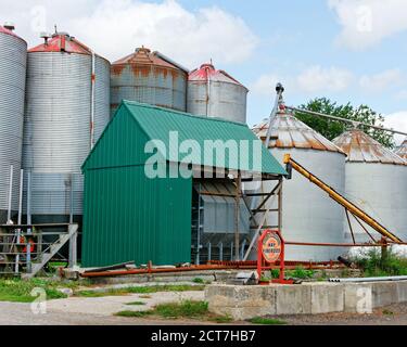 Sign reading Hay and Firewood is displayed in front of two rows of metal silos on a farm. The silos are visibly weathered and rusted. In the backgroun Stock Photo