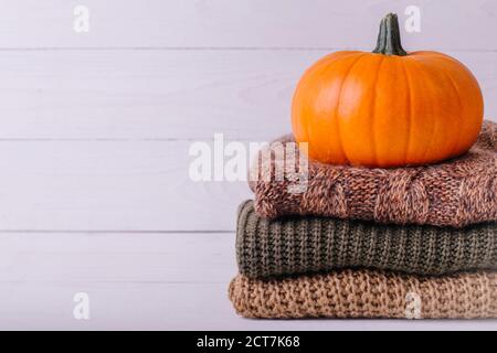 A pile of warm knitted sweaters on white wooden background with pumpkin, knitwear, place for text, Autumn sale concept. Copy Space. Stock Photo