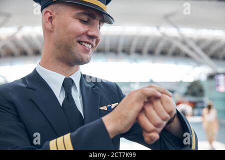 Cheerful male pilot looking at wristwatch and smiling Stock Photo