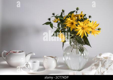 A bouquet of yellow jerusalem artichoke in a transparent vase on against white background on the table Stock Photo