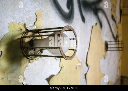 An Old Lightbulb Surrounded by Metal Bars on a Damaged Wall in an Abandoned Building Stock Photo