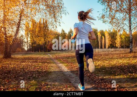 Runner training in autumn park. Young woman running at sunset in sportive clothes. Active lifestyle. Back view