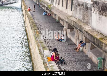 Tourists and Parisians in the evening enjoy the beauty of the Seine embankment, stroll, rest, drink and eat on the banks of the Seine in the center of Stock Photo