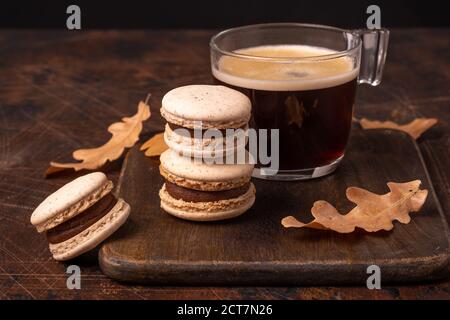 Glass cup of coffee and chocolate macarons on wooden background. Cozy autumn composition - Image Stock Photo