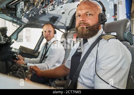 Serious bearded pilot sitting in the cockpit of passenger aircraft Stock Photo