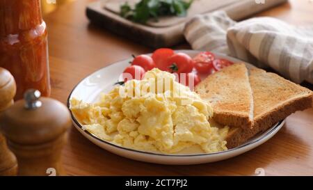 Scrambled eggs with toasted bread on plate, wooden table background. Tasty breakfast Stock Photo