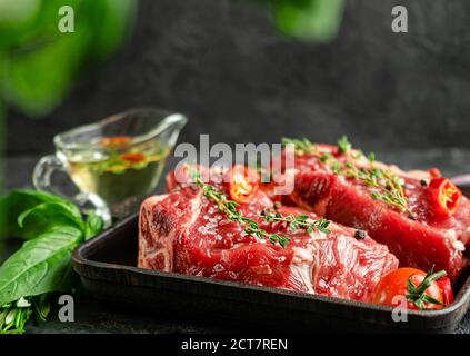 Raw veal steaks on grill pan with herbs and spicy oilive oil. Food preparation concept. Copy space Stock Photo