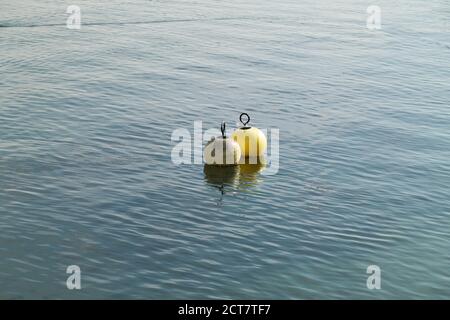 two water buoys floating in the water one white the other yellow plastic remains hang on the yellow buoy during the day in good weather without people Stock Photo