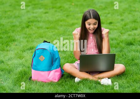 happy girl sitting on green grass with laptop. Start up. child playing computer game. back to school. education online. knowledge day. kid learning private lesson. blogging. Stock Photo