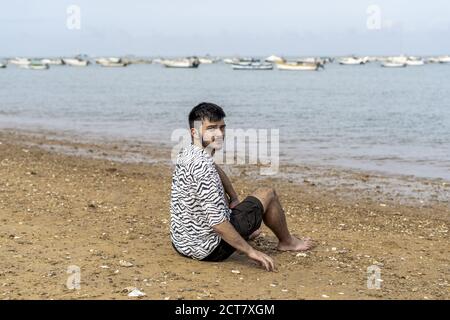 Hispanic man sitting on the shore with the view of the sea in the background Stock Photo