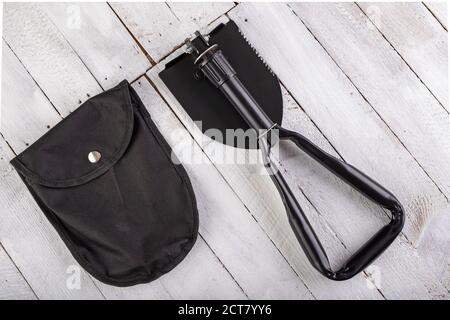 Black military shovel on a wooden table. Military accessories for excavating anti-personnel mines. White background. Stock Photo