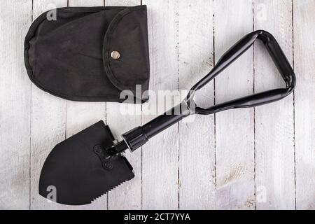 Black military shovel on a wooden table. Military accessories for excavating anti-personnel mines. White background. Stock Photo