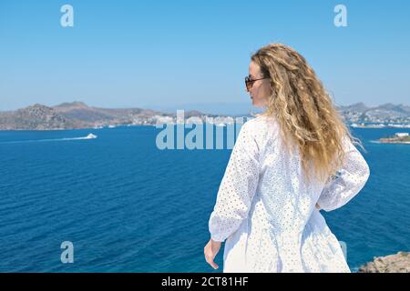 Beautiful woman from back in white dress sunglasses on white terrace of villa hotel resort looking at Sea View Stock Photo