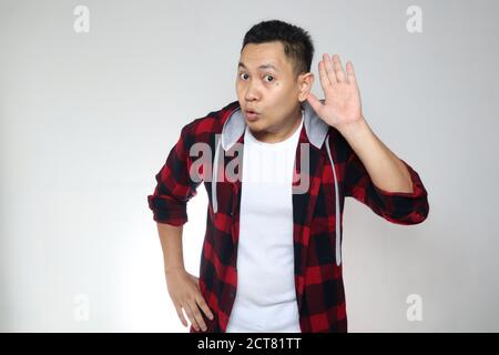 Young asian man listen whispers with funny face. Curious. Intently listen in on juicy gossip. Conversation news, privacy violation concept Stock Photo