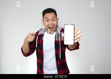Portrait of young young Asian man presenting smart phone mockup with happy cheerful expression, pointing Stock Photo