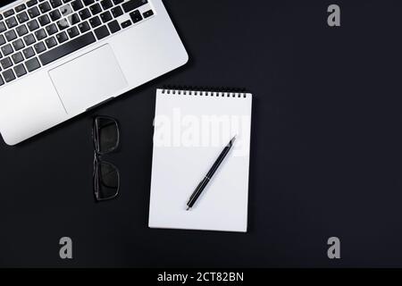 Black office desk with laptop, glasses and pen. Top view  Stock Photo