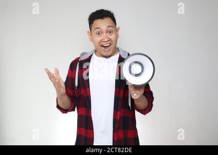Young Asian man making announcement, marketing advertisement concept, Smiling expression using megaphone, over white background Stock Photo