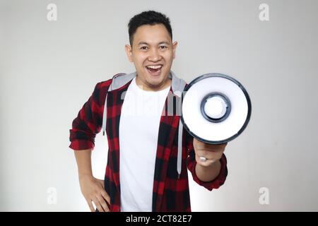 Young Asian man making announcement, marketing advertisement concept, Smiling expression using megaphone, over white background Stock Photo