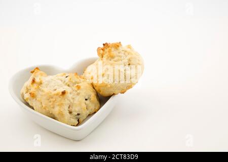 Freshly baked, hot drop biscuits made with raisins, walnuts, and yoghurt placed in heart shaped dish on white background Stock Photo