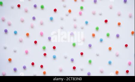 Many small bright colored pom-poms on a white background, top view, flat lay. Background concept for a holiday, a happy birthday. Stock Photo