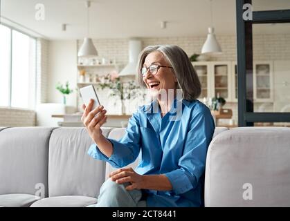Happy mature old woman holding smartphone using mobile phone app for video call. Stock Photo