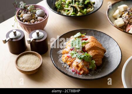Scrambled eggs & croissant on cafe table with soft natural morning light. Stock Photo