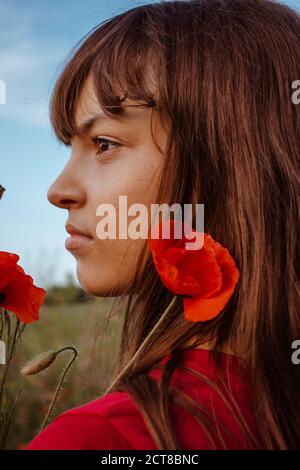 A young white teen girl portrait close-up in profileon nature meadow with red blooming poppies flowers bouquet Stock Photo