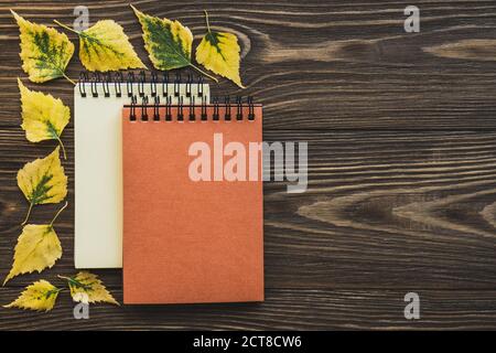 Two notepads in a frame of yellow leaves on a wooden background. Creative flat lay autumn composition. Top view, copy space. Mock up. Stock Photo