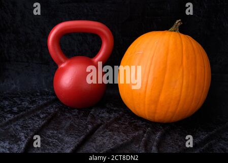 Fall fitness, orange pumpkin and red kettlebell, on a black velvet background Stock Photo