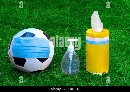 A soccer ball, football with a face mask, hand sanitizer and disinfecting wipes on a green grass. Concept football soccer in pandemic, covid-19 or cor Stock Photo