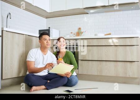 Young Asian Adult Couple Sitting on Floor and Planning New Home Design Stock Photo