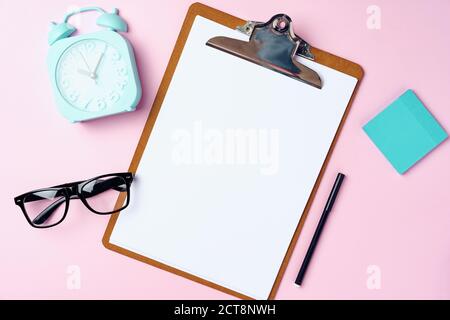 Clipboard with blank sheet of paper and alarm clock on pink Stock Photo