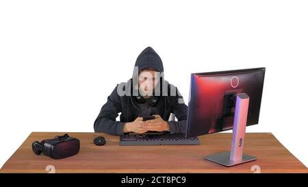 Hooded hacker using laptop and smartphone on white background. Stock Photo