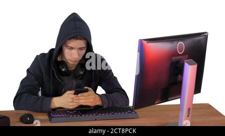 Hooded hacker using laptop and smartphone on white background. Stock Photo