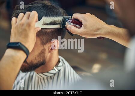 Skillful hair-stylist using electric hair clipper to cut hair Stock Photo
