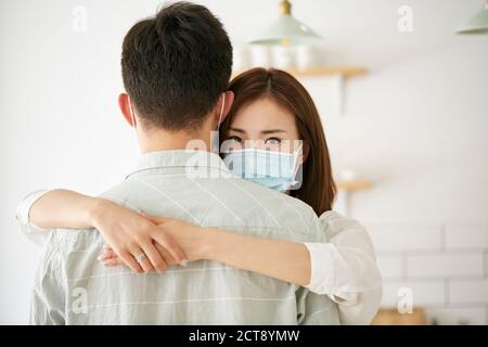 young asian woman wearing mask hugging husband looking at camera