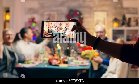 Girl taking a family portrait with her phones while celebrating christmas. Traditional festive christmas dinner in multigenerational family. Enjoying xmas meal feast in decorated room. Big family reunion Stock Photo