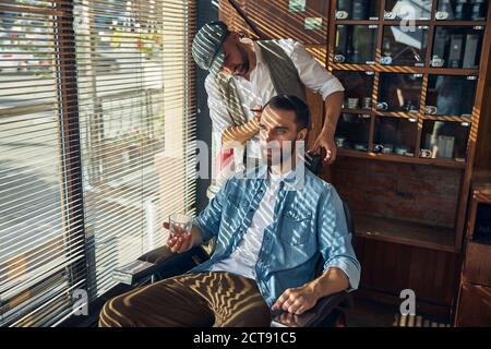 Happy young man with a glass of liquor in a hair salon Stock Photo