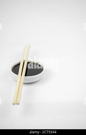 soy sauce in a small white bowl and bamboo chopsticks, isolated on white Stock Photo