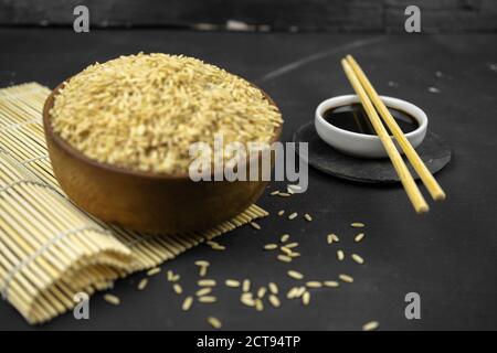 brown rice in a wooden bowl on bamboo mat, asian kitchen background on black Stock Photo