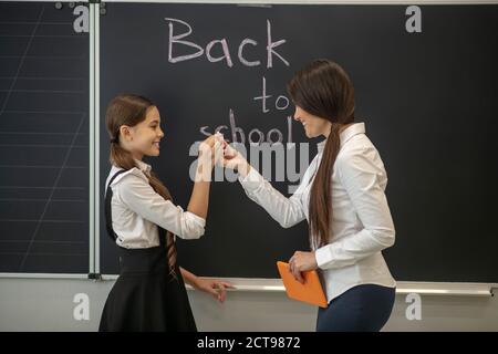 Schoolgirl and her teacher standing near blackboard and smiling Stock Photo
