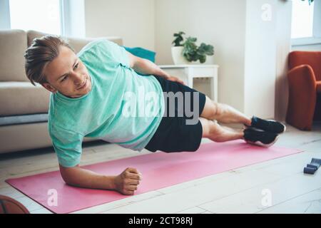 Caucasian blonde fit man doing side plank at home on the floor while having a fitness session Stock Photo