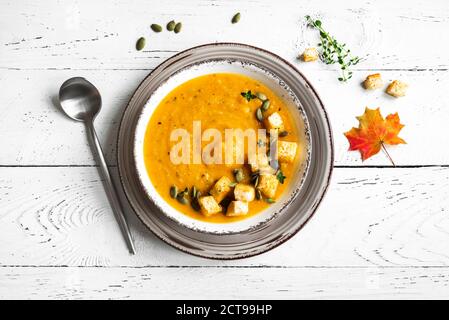 Pumpkin soup with croutons and roasted pumpkin seeds on white wooden table, top view, copy space. Seasonal autumn food - Spicy pumpkin and carrot soup Stock Photo