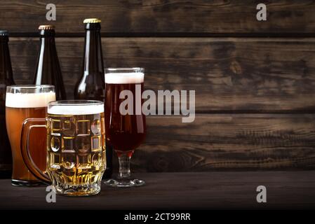Various sorts of draft beer in bottles, glasses and mug on wooden table, copy space. Fresh brewed beer. Stock Photo