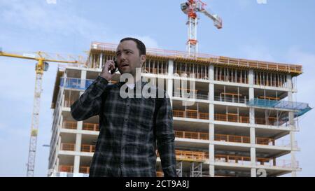 Young casual man talking on the phone near construction site. Stock Photo