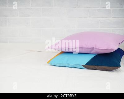 Colorful pillows, decorative pillows pink and blue on a white bedspread against a brick wall. Comfort and convenience at home Stock Photo