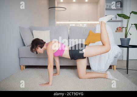 Fitness girl in athletic workout clothes training indoor home, uses headphones and personal trainer online. Interior room skandi Stock Photo