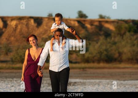 Portrait of happy multiracial family with little biracial son. Parents with toddler son walking on the beach