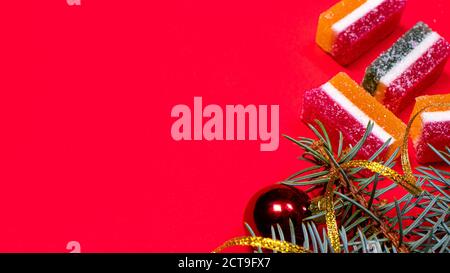 Marmalade and spruce twig with a ribbon and a toy on a red background. A banner on a red background with a place for copyspace text Stock Photo